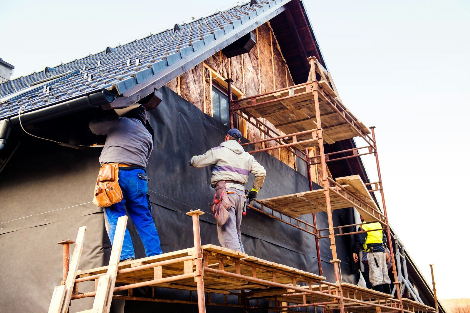 Contractors fitting external wall insulation boards onto a house with scaffolding in place.
