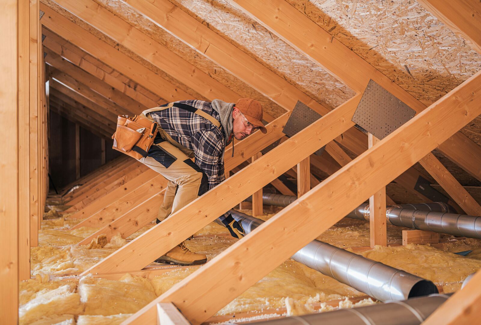 Side-by-side photograph of an Irish attic before insulation (bare rafters, exposed brick gable) and after fitting yellow mineral wool insulation between and across the rafters.