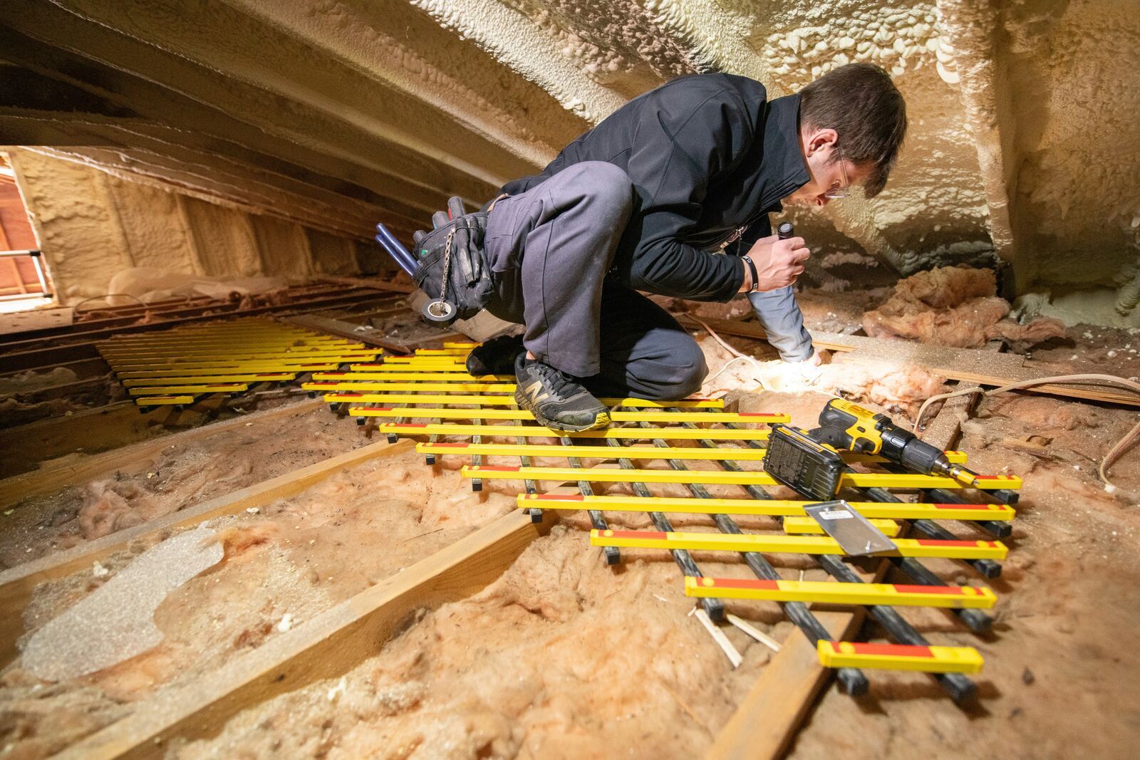 Two installers carefully unrolling mineral wool insulation across attic joists.