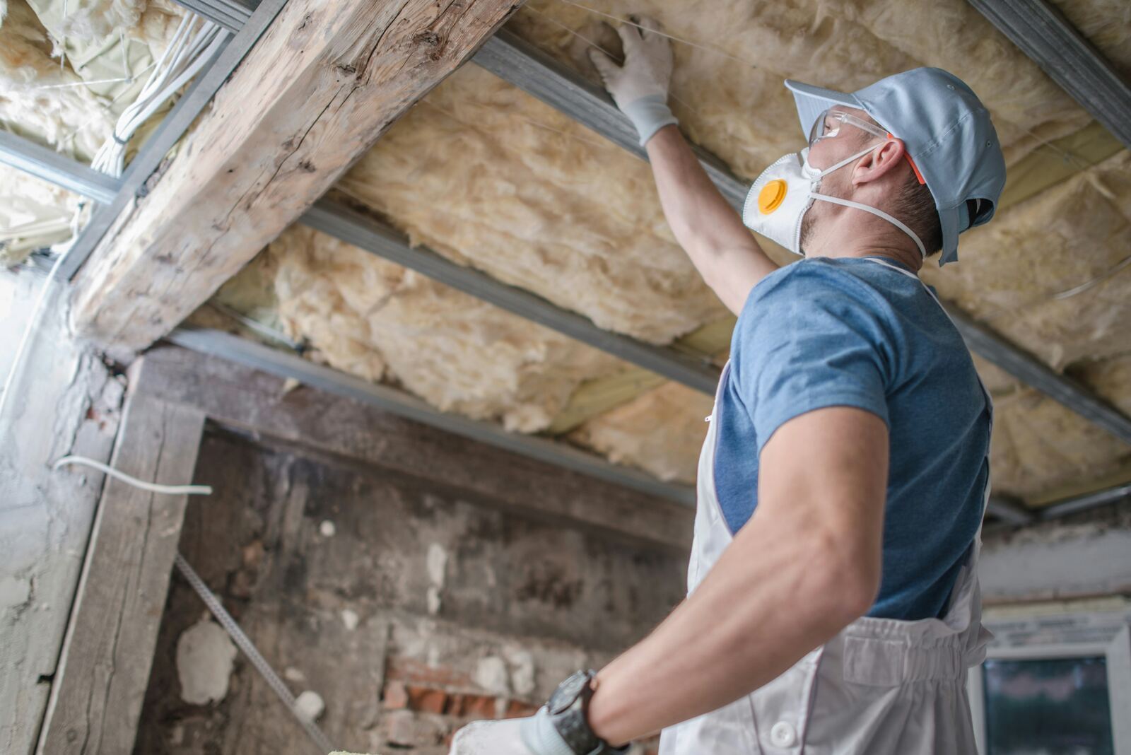 Installers fitting mineral wool loft insulation between joists.